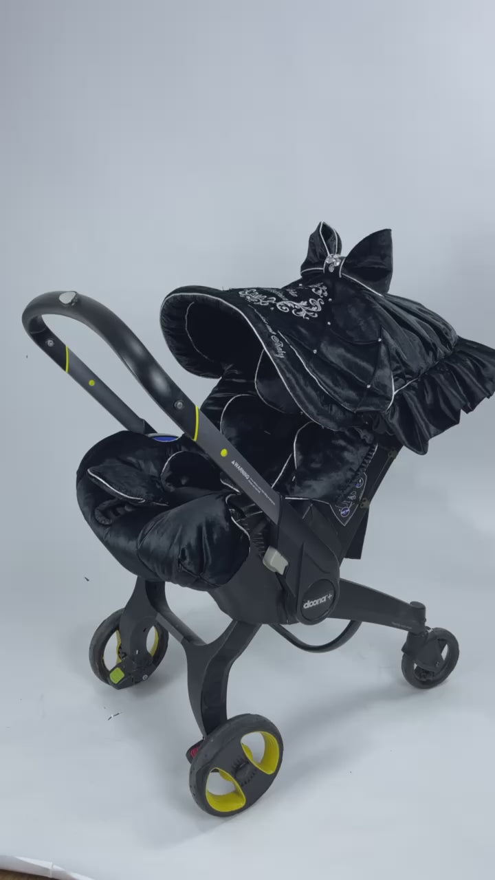 Angled side view of a luxury black velvet stroller cover set featuring quilted canopy with embroidered visor, rhinestone bow and layered ruffle detailing.