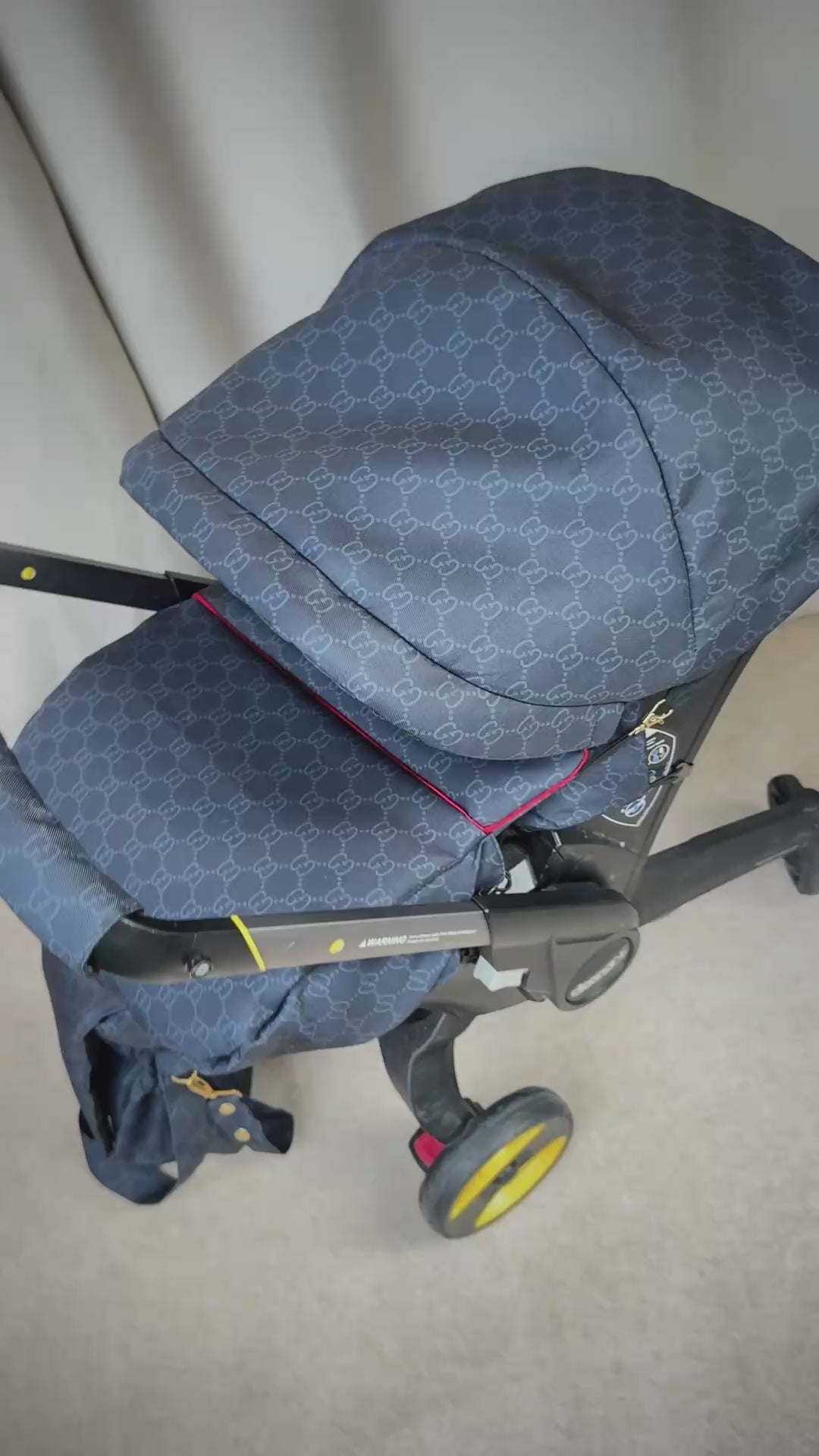 Black monogram Doona+ car seat cover with red piping trim, installed on Doona+ stroller, side view video preview.