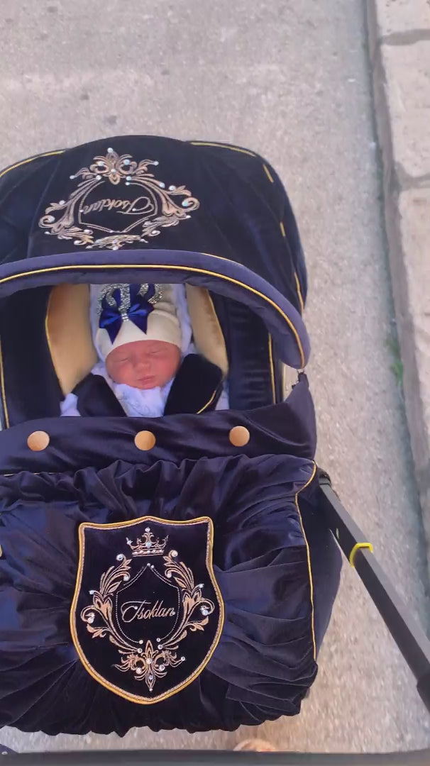 Newborn baby in Royal Blue velvet Doona Plus car seat cover with gold trimming, gold buttons and embroidered crest.
