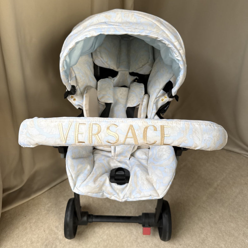 Baby stroller with 'Versace' branding on a beige background
